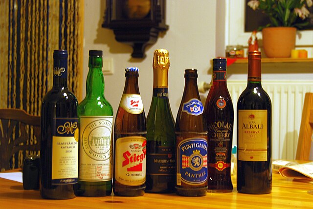 Różnorodne butelki alkoholi ustawione w linii na drewnianym stole w przytulnym wnętrzu.