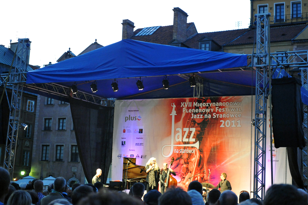 Muzyk z mikrofonem występujący na scenie festiwalu jazzowego, z publicznością w tle.