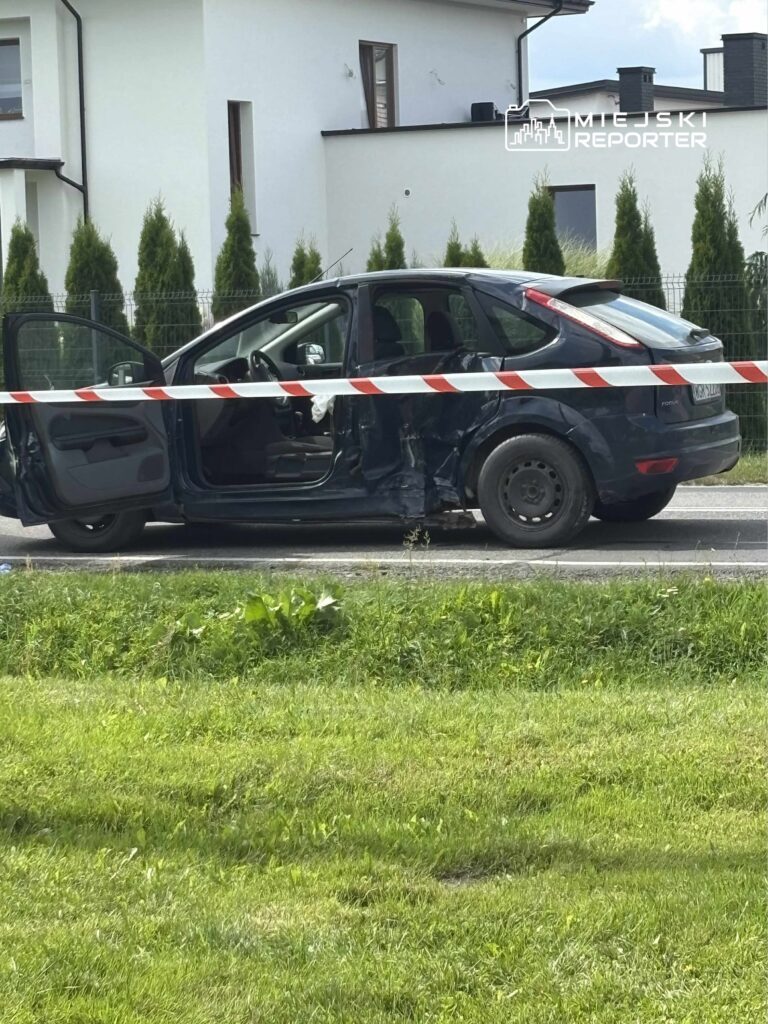 Czarny samochód osobowy z otwartymi drzwiami, stojący na poboczu drogi, z widocznymi uszkodzeniami.