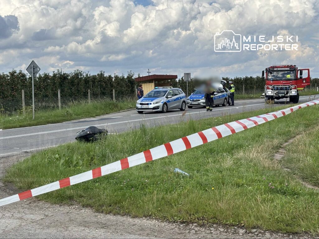 Na drodze stoi policyjny radiowóz z otwartą maską, obok straż pożarna oraz zabezpieczony pas ruchu z taśmą.