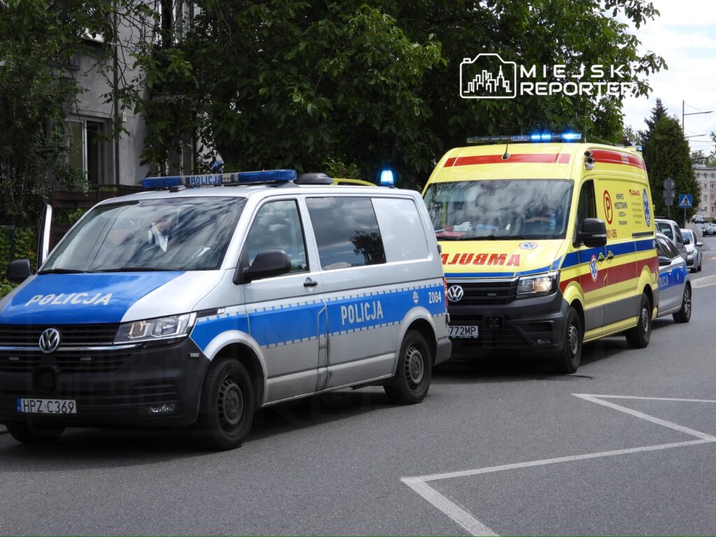Policyjny pojazd oraz ambulans z włączonymi sygnałami świetlnymi zatrzymane na ulicy w miejskim otoczeniu.