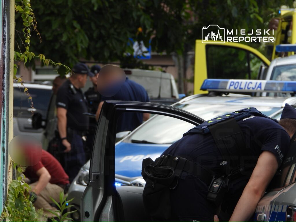 Grupa policjantów prowadzi działania interwencyjne w pobliżu zaparkowanych radiowozów.