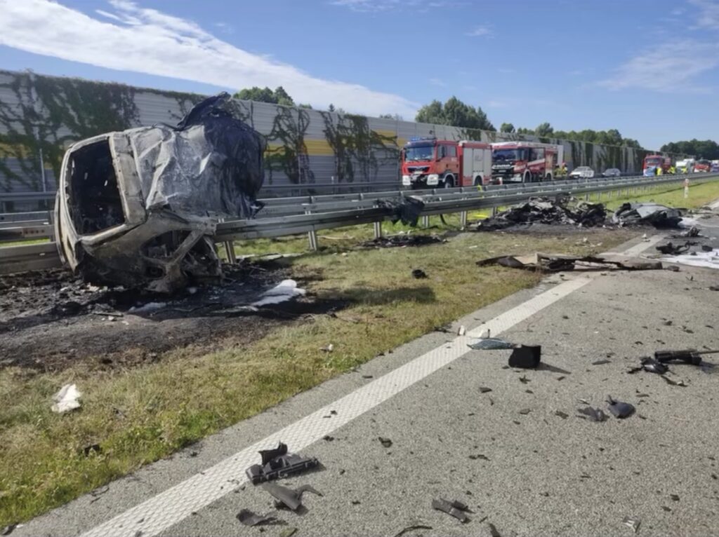Zniszczony samochód leży na poboczu drogi, obok znajdują się resztki wraku i sprzęt strażacki.