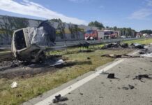 Zniszczony samochód leży na poboczu drogi, obok znajdują się resztki wraku i sprzęt strażacki.