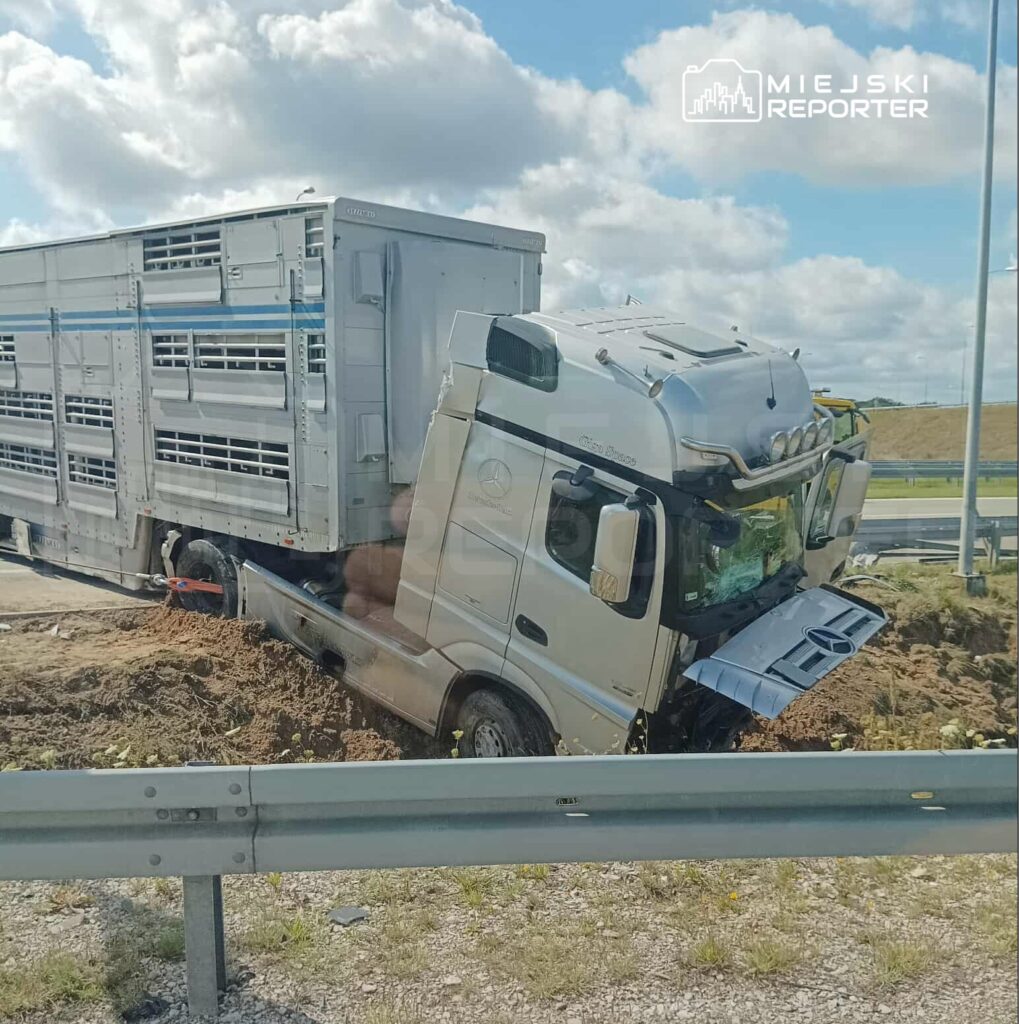 Ciężarówka z przyczepą wjechała w pobocze drogi, z przodu utknęła w ziemi, w tle widoczne chmury i zieleń.