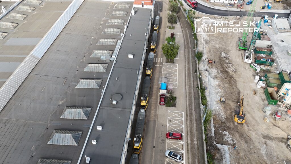 Dwa żółte pojazdy budowlane stoją na parkingu obok nowoczesnego budynku w trakcie prac budowlanych.