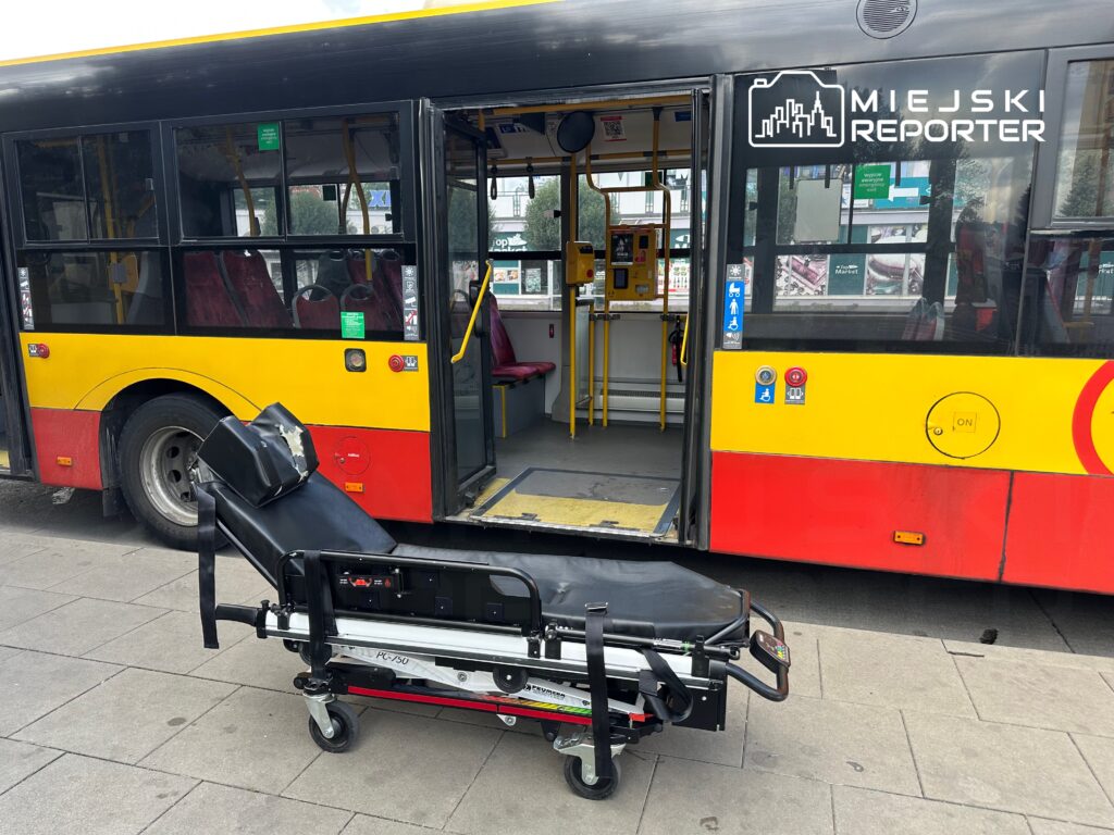 Nosze medyczne stoją przed otwartymi drzwiami miejskiego autobusu, na tle wnętrza z czerwonymi siedzeniami.