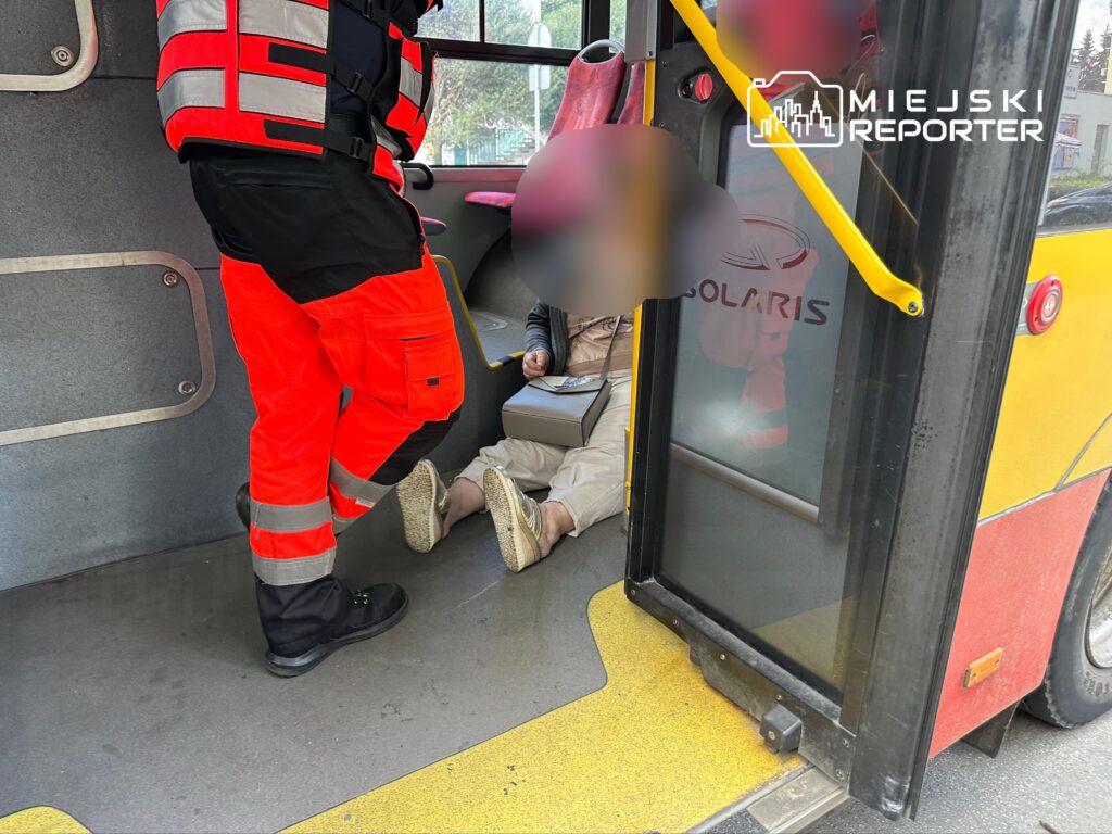 Ratownik medyczny udziela pomocy osobie siedzącej na podłodze w autobusie miejskim.