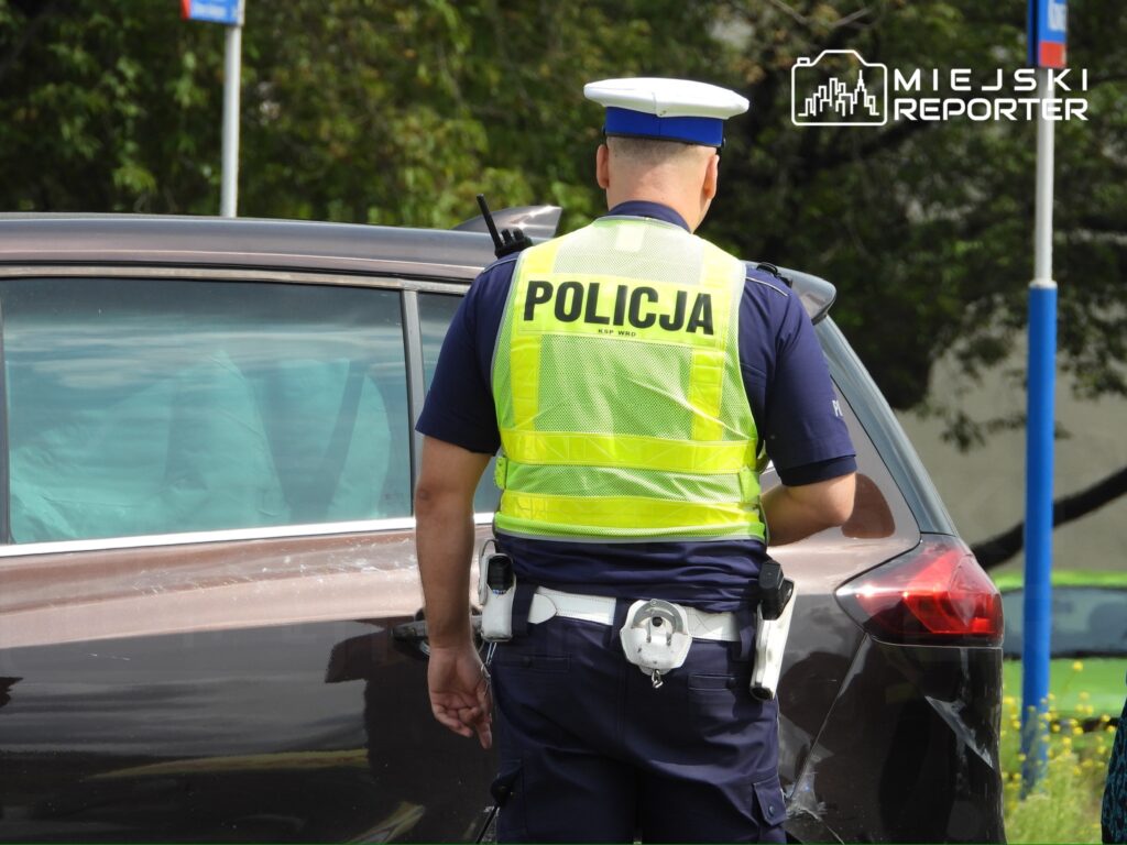 Policjant w kamizelce odblaskowej bada uszkodzony samochód na parkingu.