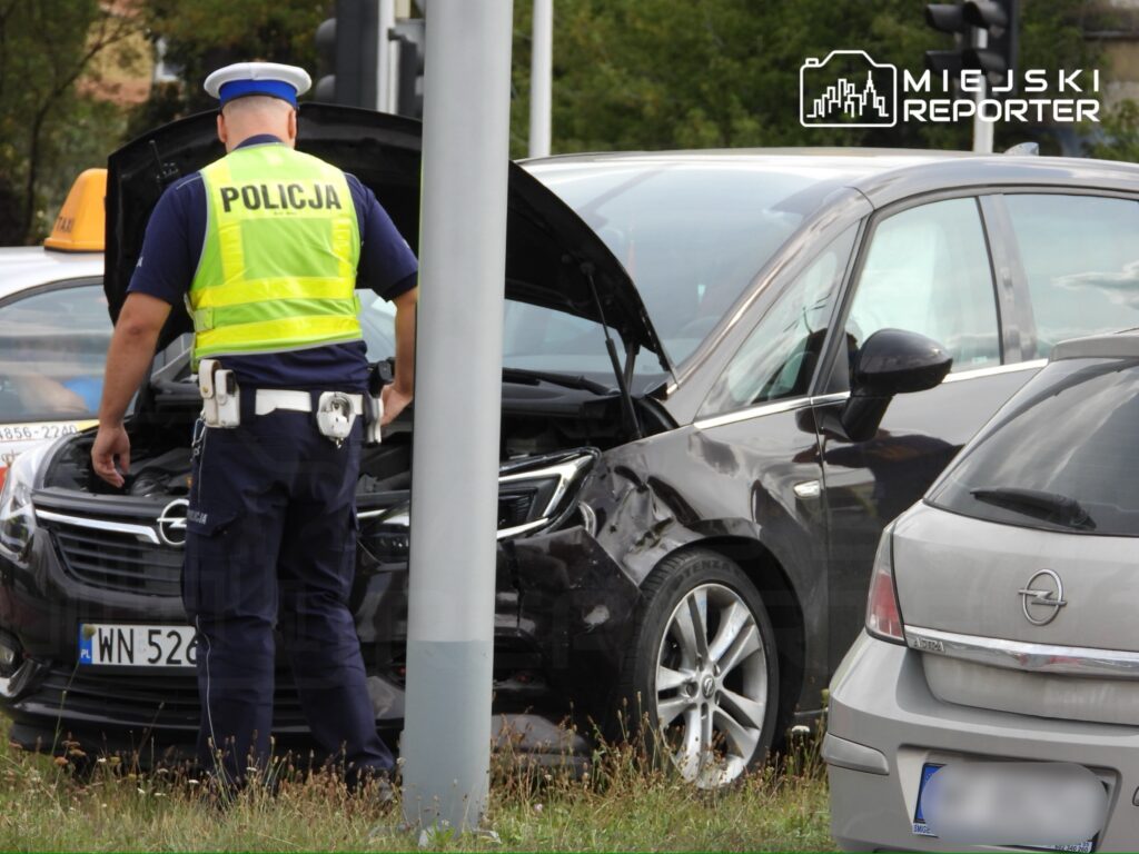 Policjant w kamizelce odblaskowej bada wypadek drogowy z udziałem dwóch samochodów osobowych na skrzyżowaniu.
