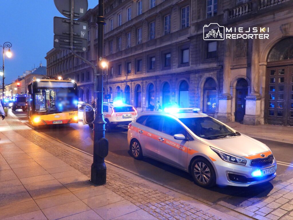 Autobus miejski zatrzymany na ulicy, obok pojazdy służb ratunkowych z włączonymi sygnałami świetlnymi.