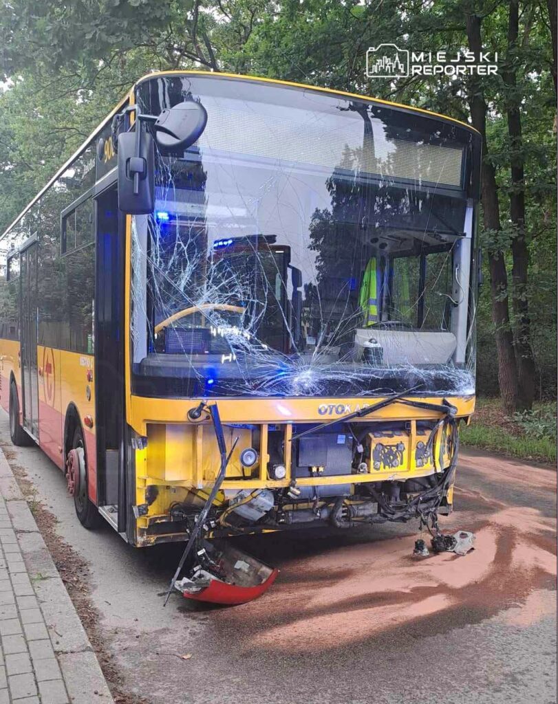 Zniszczony autobus z pękniętą szybą stoi na drodze w lesie, w pobliżu widoczna plama płynu.