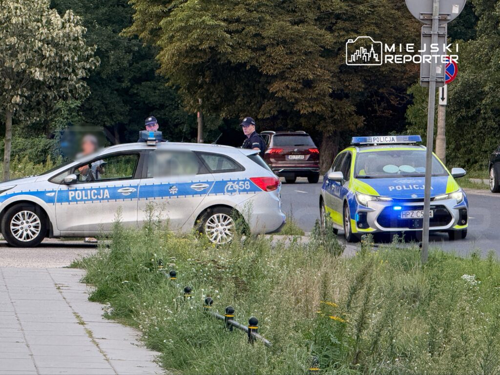 Policjanci rozmawiają z kierowcą w samochodzie osobowym podczas kontroli drogowej na miejskiej ulicy.