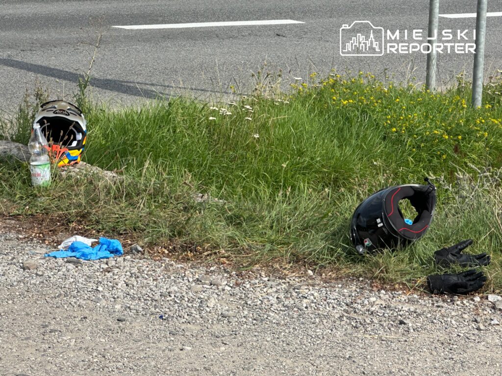 Dwa kaski motocyklowe oraz rękawice leżą na poboczu drogi, obok butelki i niebieskiego materiału.