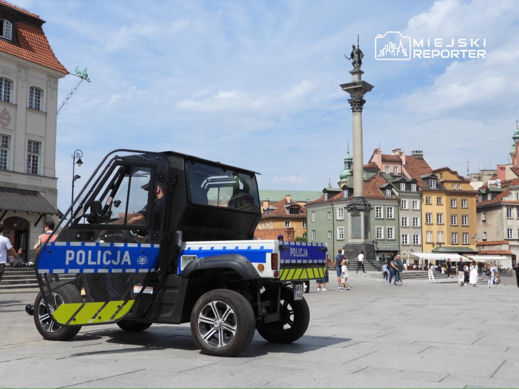 Policyjny pojazd terenowy stoi na rynku, w tle kolorowe kamienice i kolumna Zygmunta.