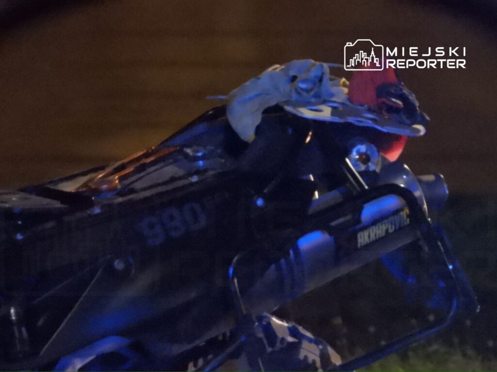 Motocykl sportowy z widocznym tłumikiem i elementami ozdobnymi w ciemnym otoczeniu nocnym.