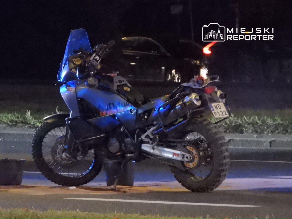 Motocykl terenowy zaparkowany na poboczu drogi, oświetlony niebieskimi światłami w nocy.