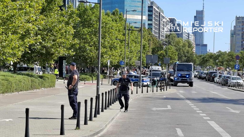 Dwóch policjantów stoi na chodniku, obserwując ruch na ulicy w tle nowoczesnych budynków.