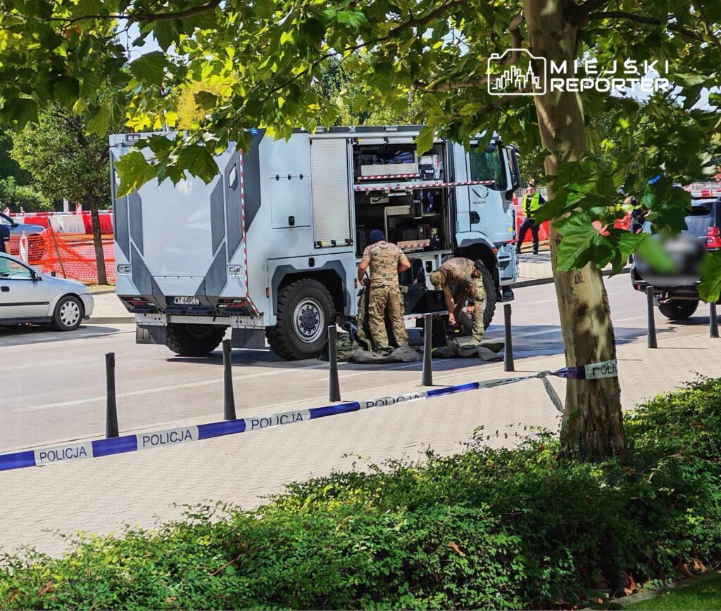 Dwaj żołnierze w mundurach rozkładają sprzęt obok policyjnego pojazdu na zatłoczonej ulicy.