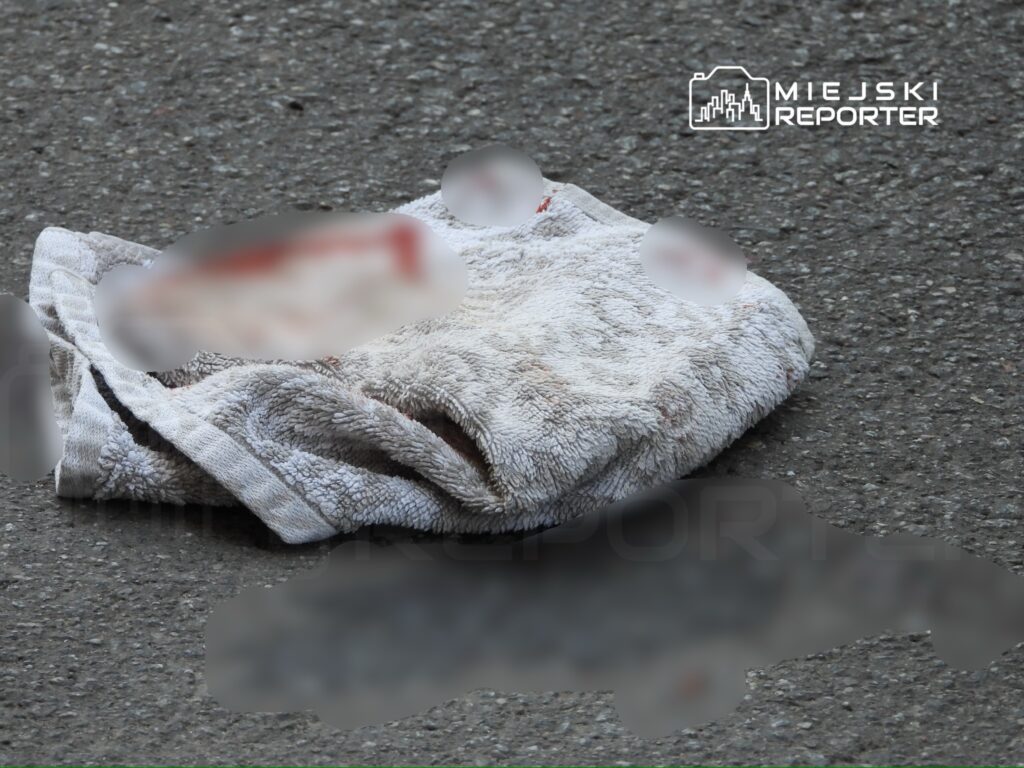 Na szarej nawierzchni leży brudny ręcznik z plamami, rozłożony w miejskim otoczeniu.