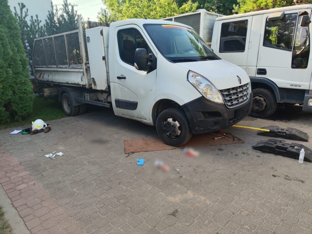 Biały samochód dostawczy unieruchomiony na podjeździe, obok leży kask strażacki i narzędzia.