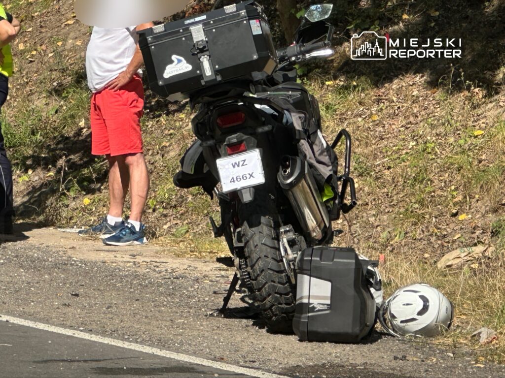 Mężczyzna w czerwonych szortach rozmawia z policjantem obok motocykla zaparkowanego na poboczu drogi.