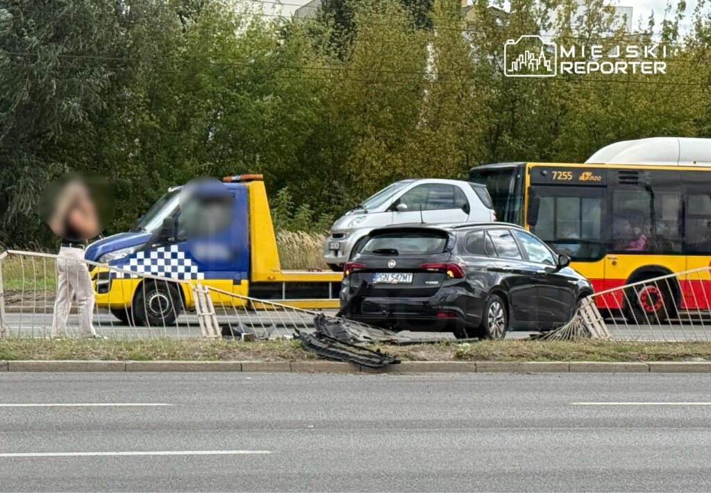 Kobieta w jasnych spodniach stoi obok uszkodzonego samochodu na poboczu drogi, obok podjeżdża laweta.