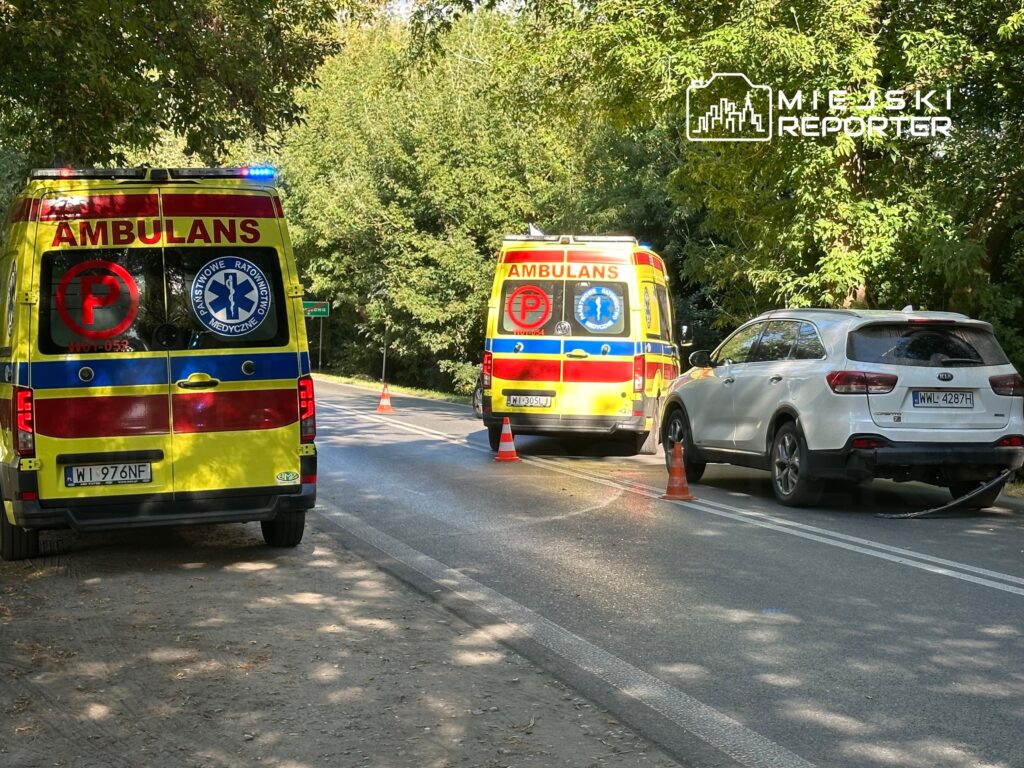 Na drodze stoją dwa karetki pogotowia z włączonymi sygnalizacjami świetlnymi, obok uszkodzony samochód osobowy.