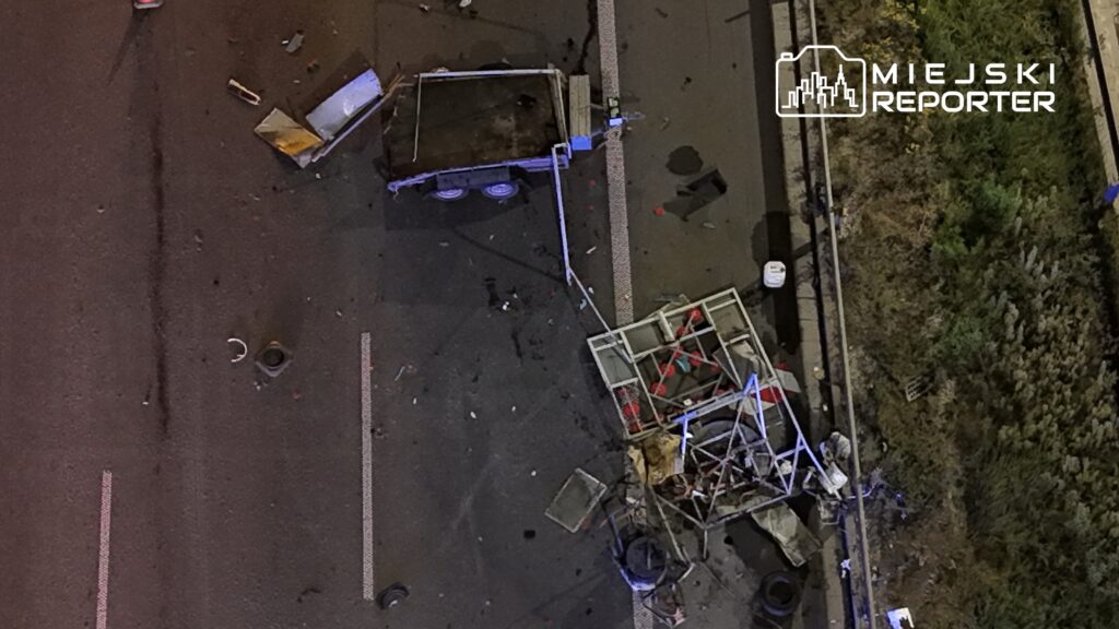 Zdemolowana przyczepa leży na jezdni, otoczona odpadkami i fragmentami materiałów budowlanych.