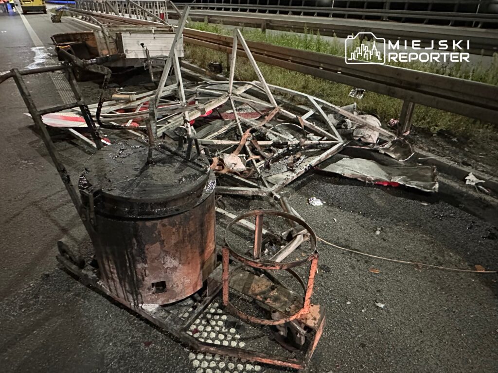 Zniszczone elementy konstrukcji leżą na jezdni, obok widoczna plama cieczy oraz fragmenty metalu.