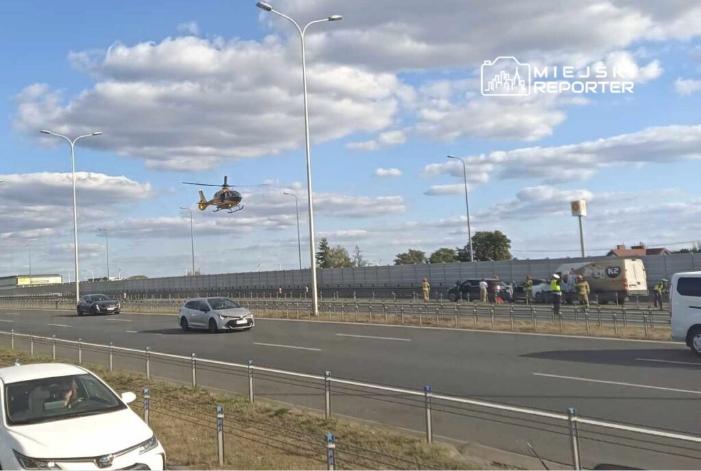 Helikopter ratunkowy unosi się nad ruchem drogowym, podczas gdy służby ratunkowe zajmują się wypadkiem na jezdni.
