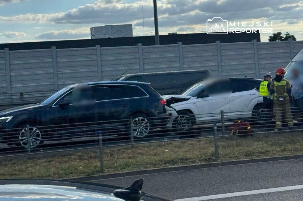 Wielki wypadek drogowy z udziałem dwóch samochodów osobowych na pasie ruchu, obok grupy ratowników i policji.