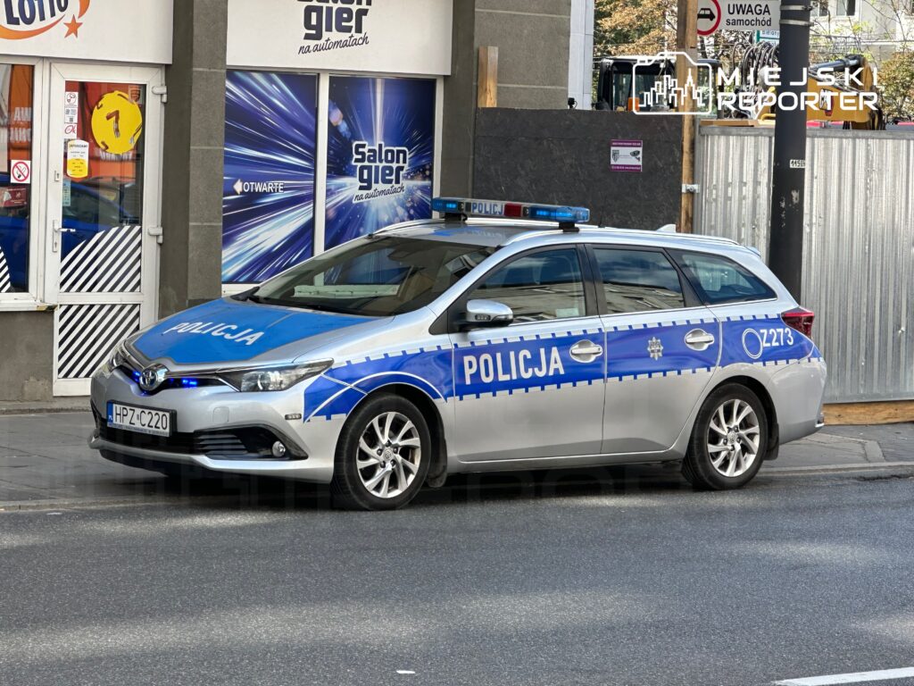 Radiowóz policyjny zaparkowany przy salonie gier, z włączonymi sygnalizatorami świetlnymi.