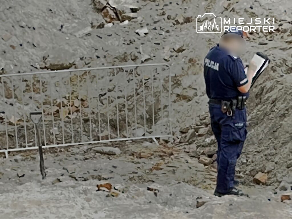 Policjant w niebieskim mundurze dokonuje oględzin terenu budowy, notując obserwacje w notatniku.