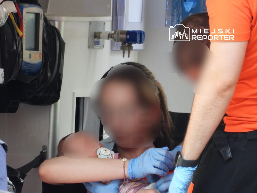 Kobieta z dzieckiem na rękach otrzymuje pomoc medyczną od ratownika w ambulansie.