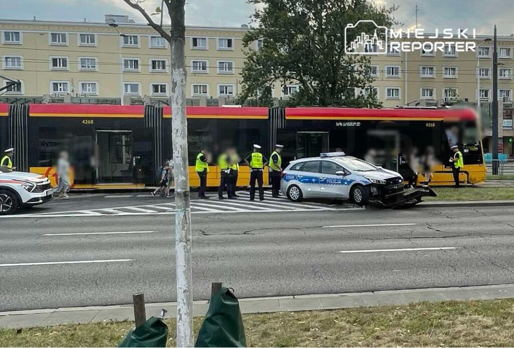 Policjanci prowadzą czynności na miejscu wypadku tramwaju z samochodem osobowym na ruchliwej ulicy.