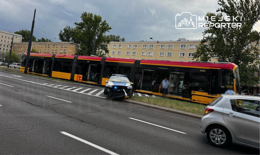 Tramwaj z numerem 4268 zatrzymany na przystanku, obok policyjny radiowóz z włączonymi sygnałami świetlnymi.