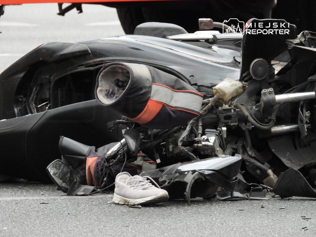 Zniszczony motocykl leży na drodze, obok widoczny jest jeden sportowy but.