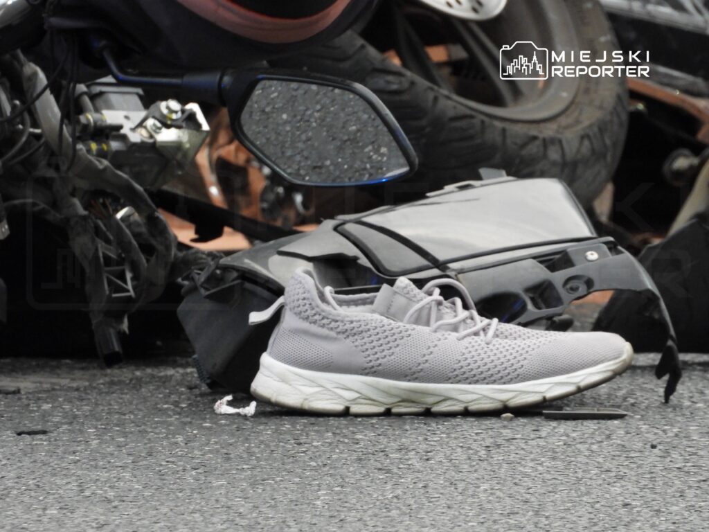 Szary but sportowy leży na drodze obok uszkodzonego motocykla i fragmentów pojazdu.