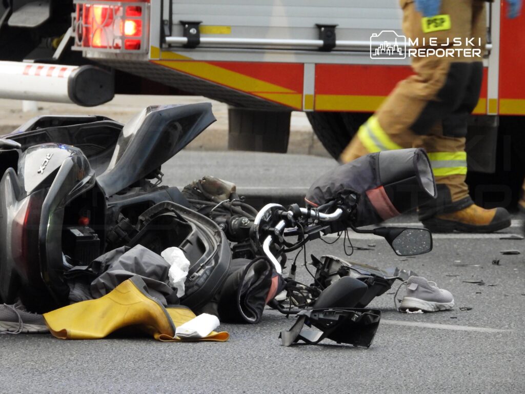 Rozbite motocykle leżą na jezdni obok odzieży ochronnej i sprzętu, w tle widać pojazd strażacki.