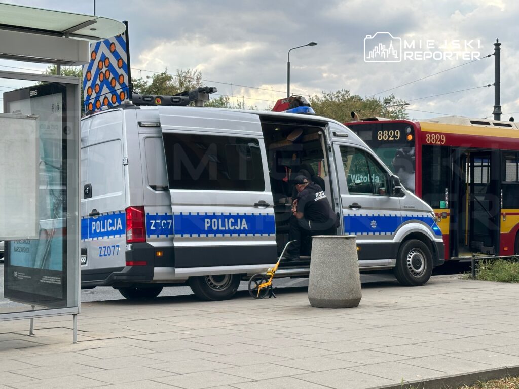Policyjna furgonetka zatrzymana na przystanku, policjant sprawdzający dokumenty w środku, obok autobus komunikacji miejskiej.