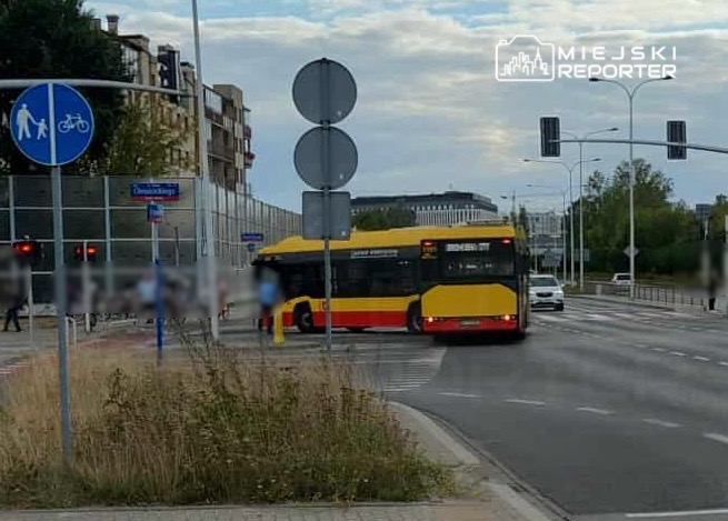 Autobus w żółto-czerwonym malowaniu skręca w prawo na ruchliwym skrzyżowaniu w miejskim otoczeniu.