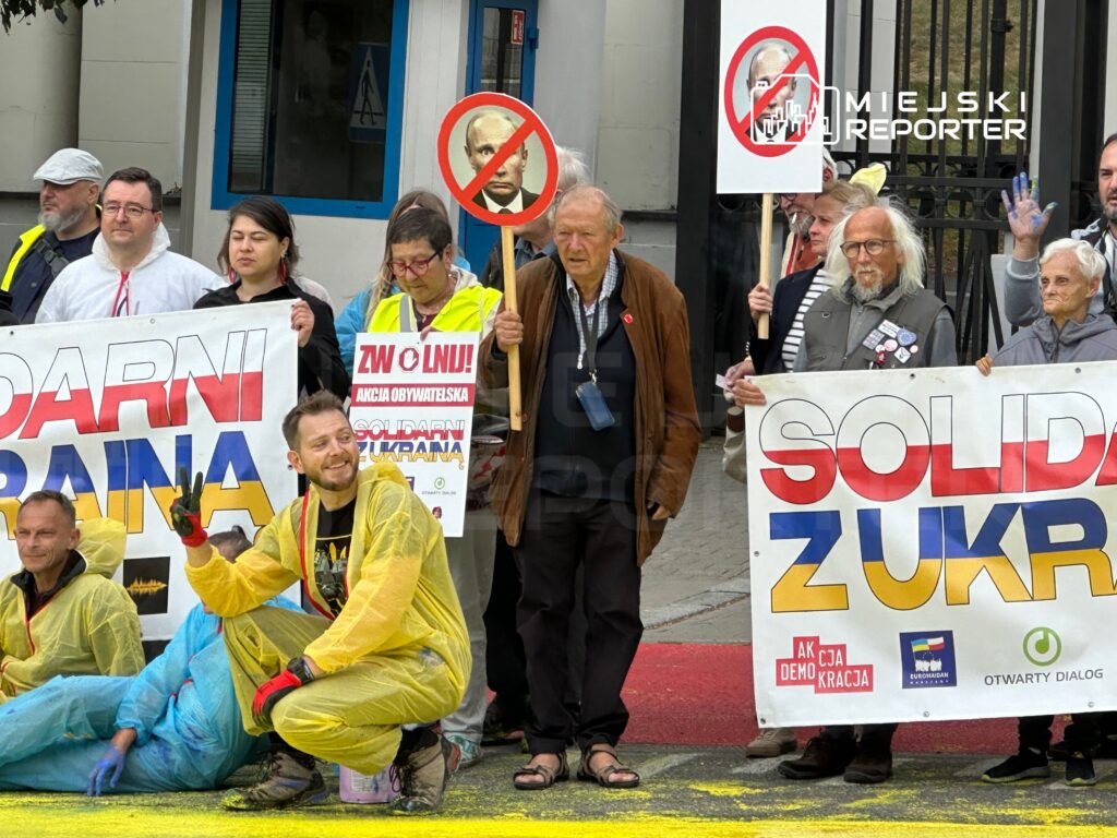 Grupa protestujących trzymająca transparenty z hasłami "SOLIDARNI Z UKRAINĄ" i "ZWOLNIĆ!", w tle budynek.