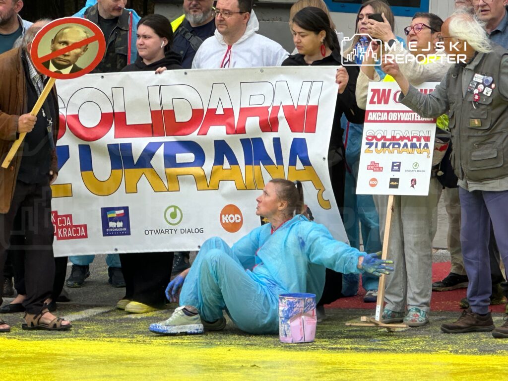 Grupa demonstrantów z transparentem "SOLIDARNI Z UKRAINĄ" uczestniczy w proteście, niektórzy trzymają plakaty.
