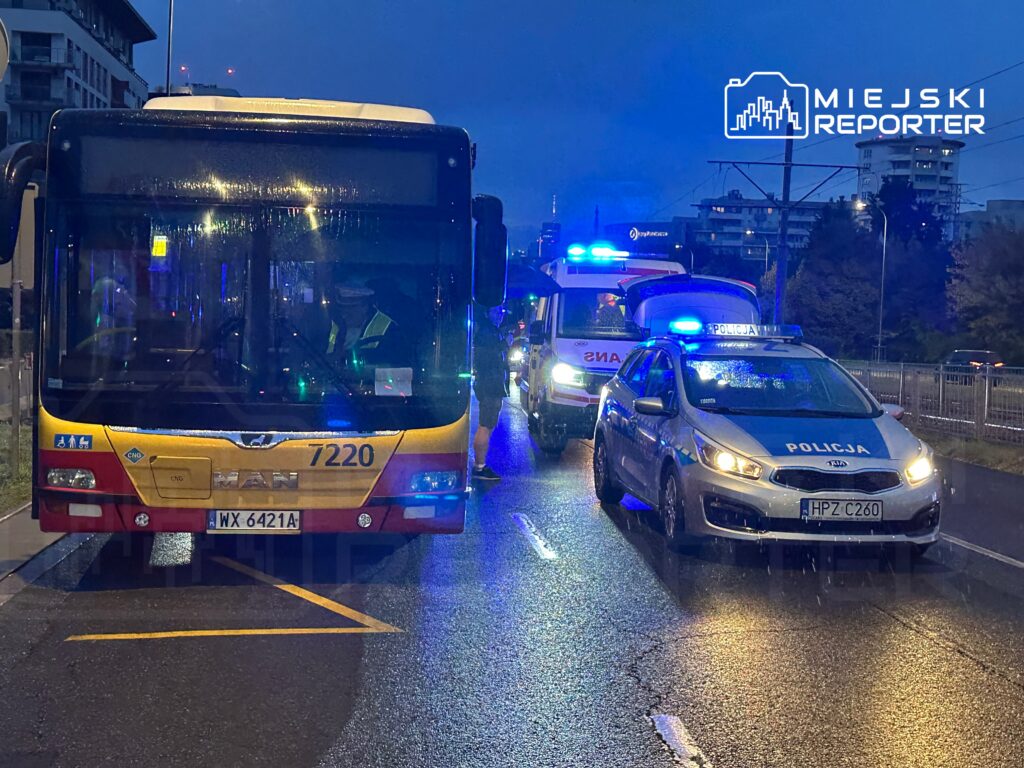 Autobus MAN z numerem 7220 zatrzymany na ulicy, obok policyjny radiowóz oraz karetka z włączonymi sygnałami.