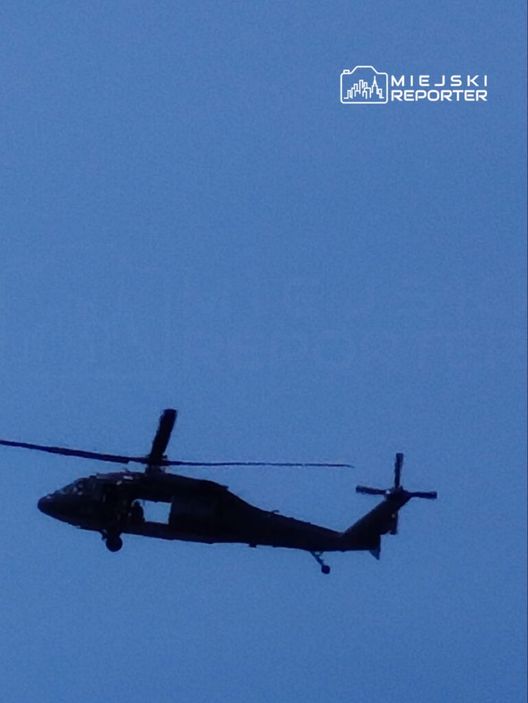 Czarny helikopter wojskowy przelatujący nad niebieskim niebem.