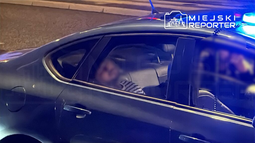 Mężczyzna leżący na tylnym siedzeniu niebieskiego samochodu osobowego, otoczonego przez niebieskie światła.