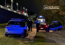 Policjanci prowadzą czynności na poboczu drogi, obok zaparkowanych radiowozów w nocy.