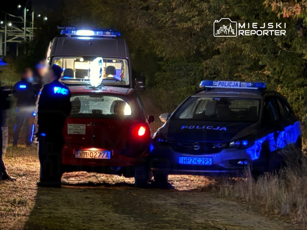Grupa policjantów w mundurach prowadzi interwencję przy dwóch samochodach na oświetlonej drodze.