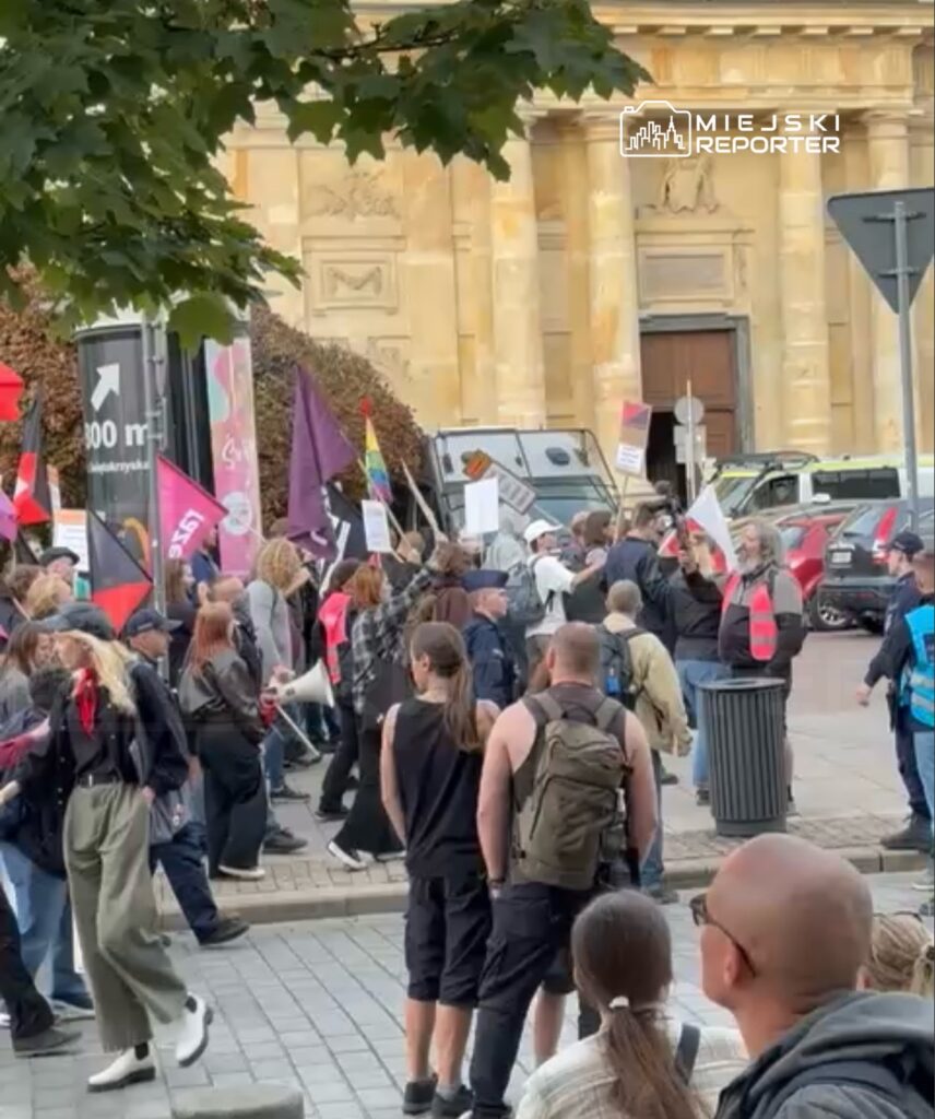 Grupa ludzi z transparentami i flagami protestuje na ulicy przed historycznym budynkiem.